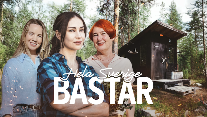 Three women standing in a forest in front of a sauna.