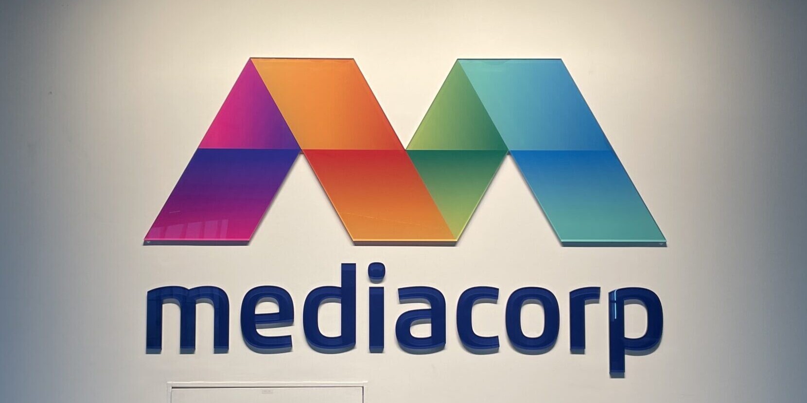 An illuminated Mediacorp logo on a plain white wall