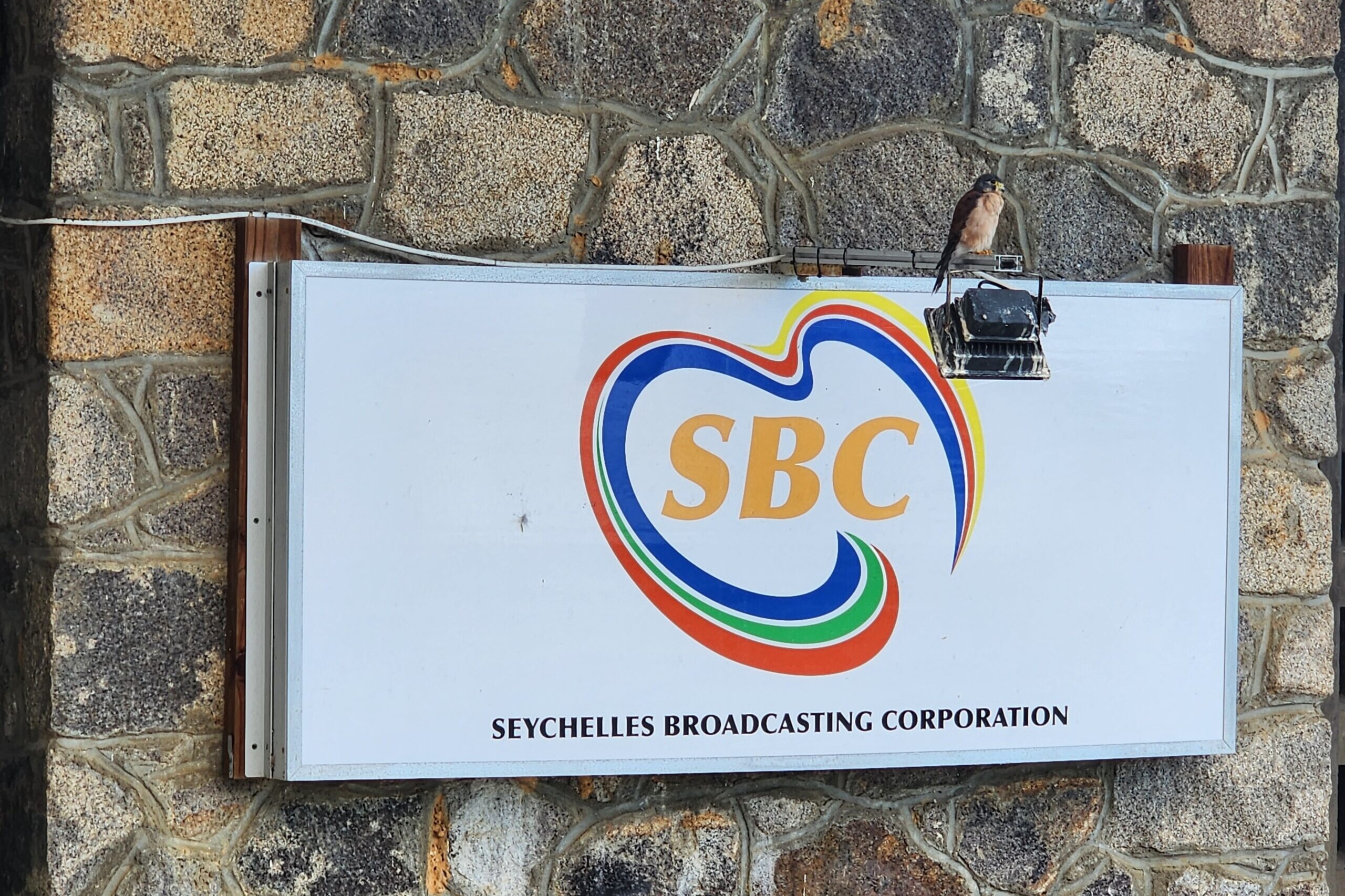 A white sign with the SBC logo on a stone wall.